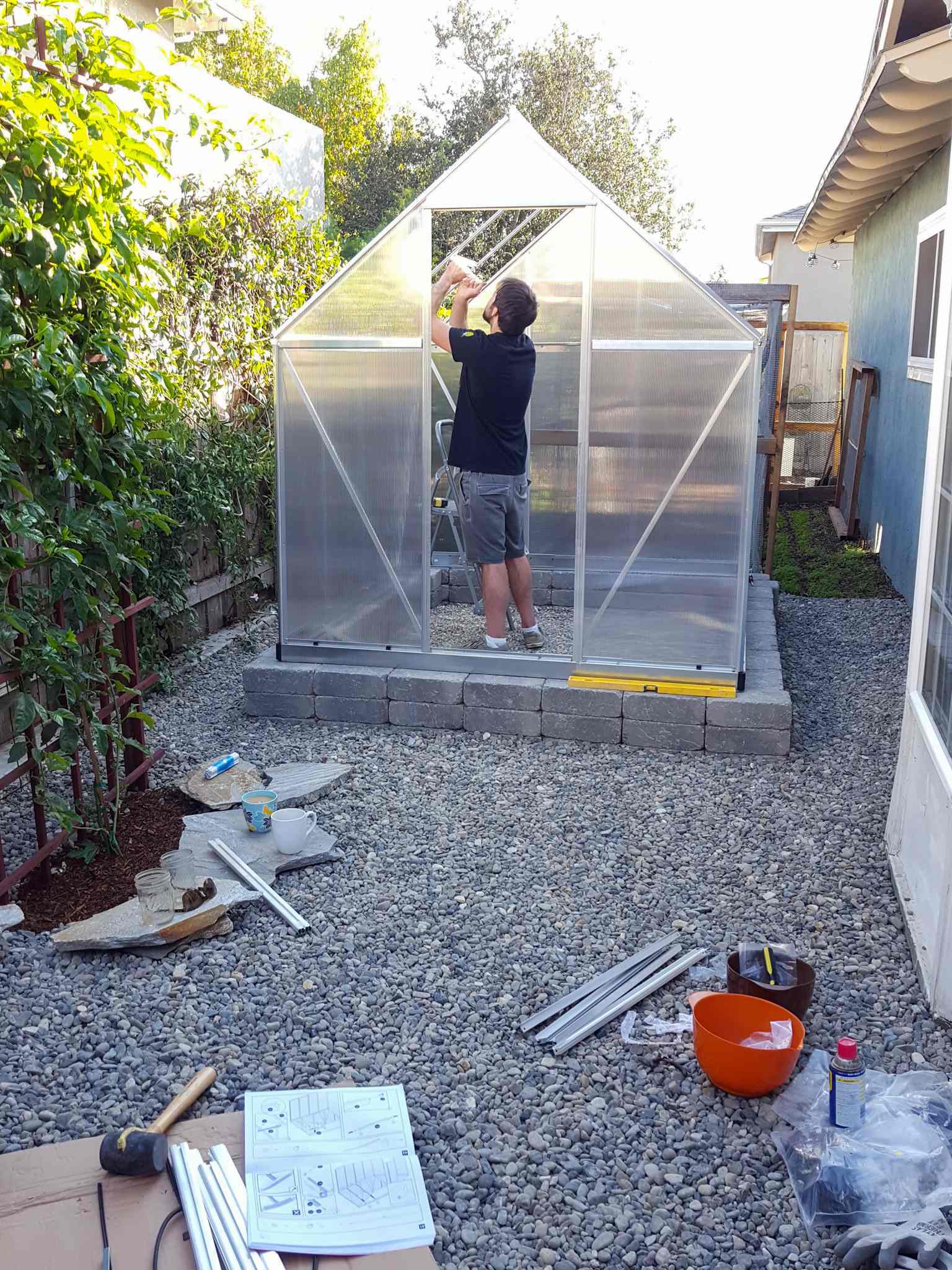 Aaron is inside the greenhouse while it is still under construction. There are tools laid here and there and there are at least two panels of the roof that still need to be installed. A greenhouse is a great use of space to start many plants by seed.