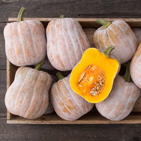 A wooden box full of butternut squash whose skin is silvery tan and the flesh is bright orange in color. 