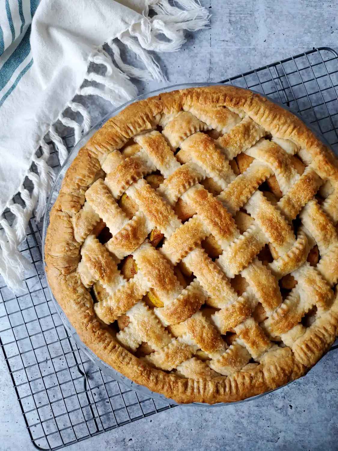 An apple pie with a latticed crust has just finished baking. The crust is golden brown and the space between the lattice pieces reveal apples below. Use this sourdough discard recipe for a delicious pie crust.