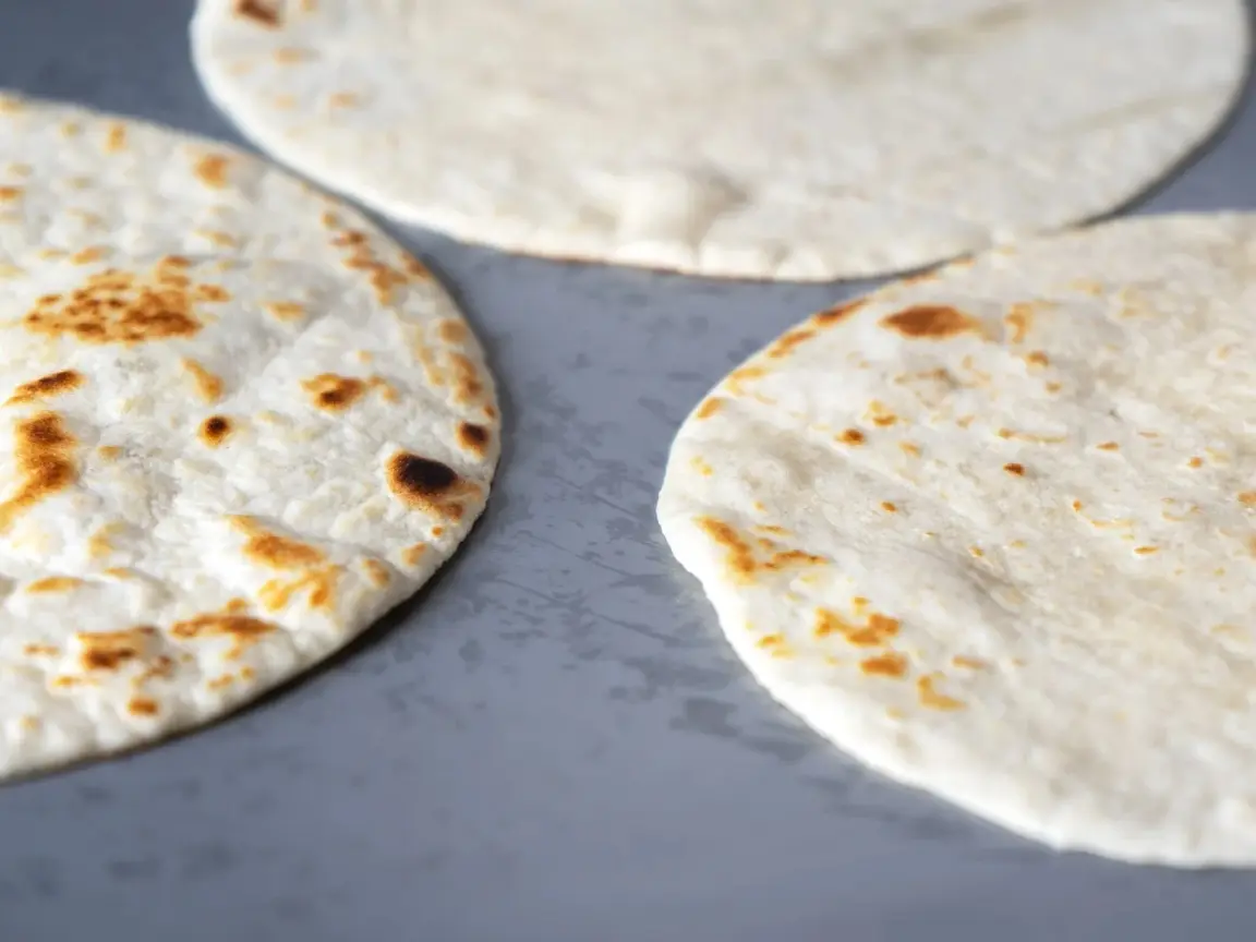 A few flour tortillas that have light brown spots here and there are sitting flat on a surface. Use sourdough discard recipes to make delicious tortillas. 