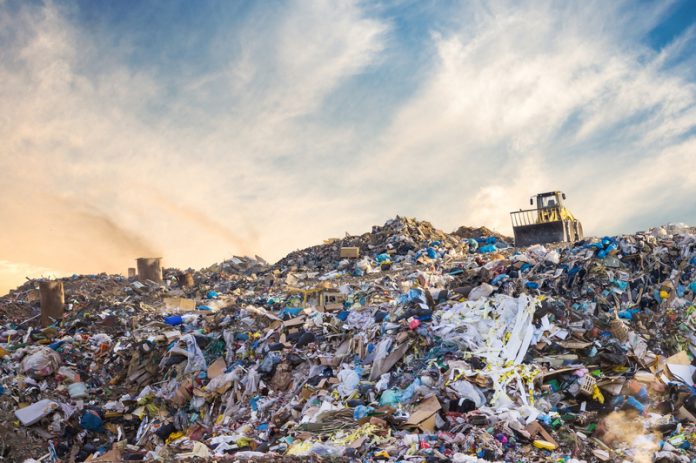 An image of a landfill with a tractor sitting on the top of the giant mountain of trash.