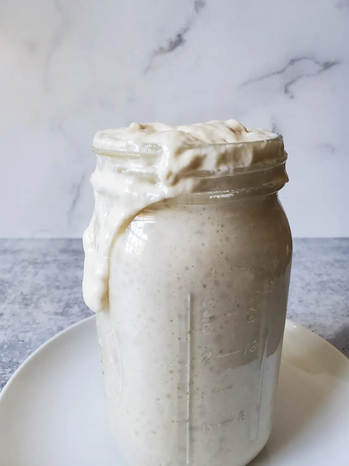 A quart mason jar is overflowing with freshly activated sourdough starter. Some of the starter is dripping down the side of the top portion of the jar. 