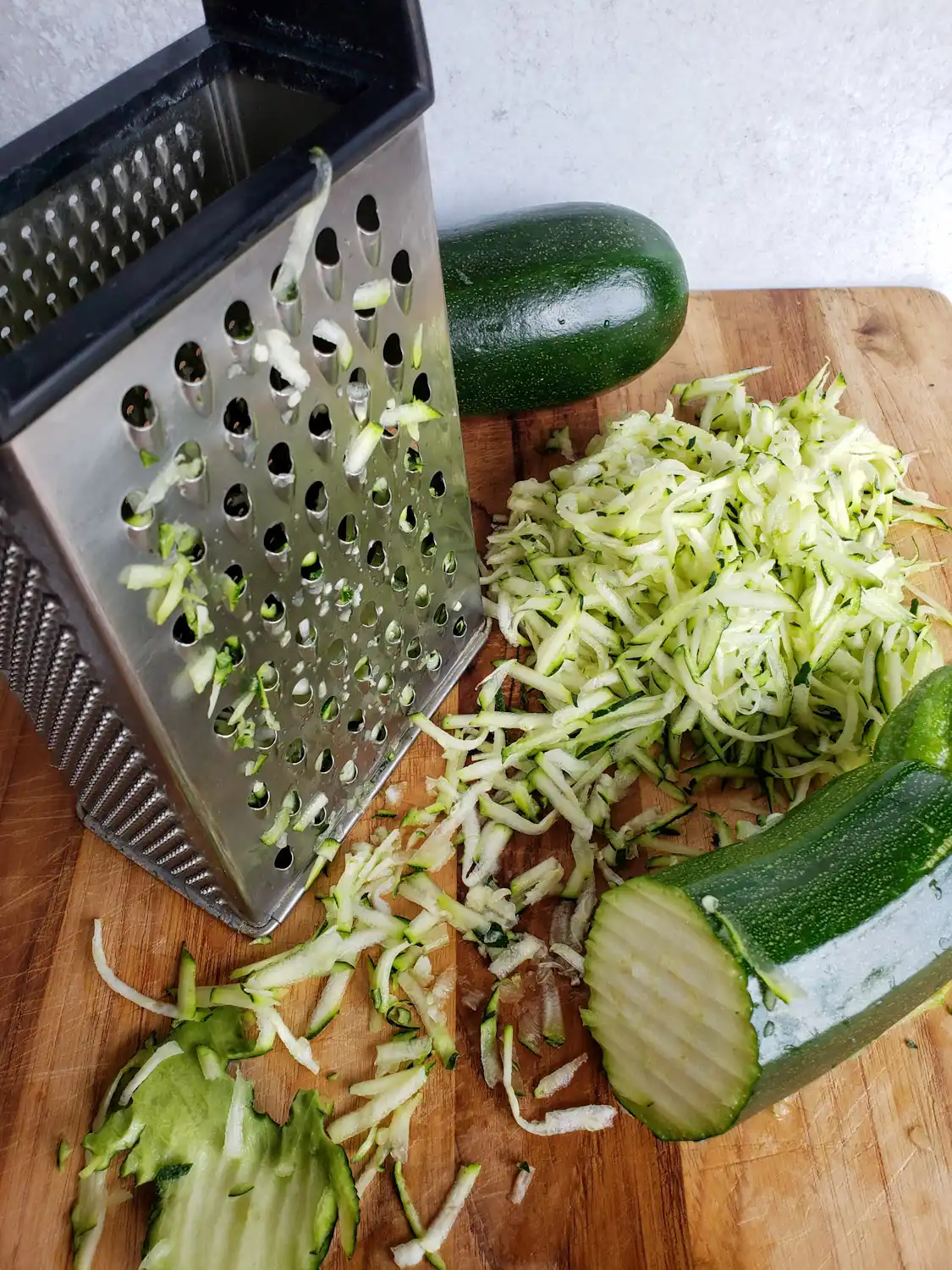 A close up image of a piece of squash that has been partially grated with a box grater. Another squash sits behind the grater with half of the squash poking out from behind. 