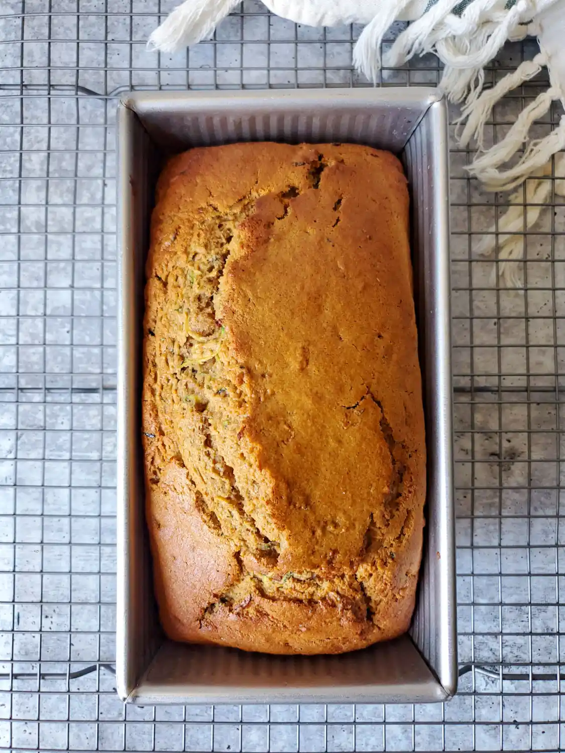 A birds eye view of a loaf of sourdough zucchini bread that has just been pulled from the oven, still sitting inside of the baking pan. The top is light brown with a nice open ear and crumb on the top. 