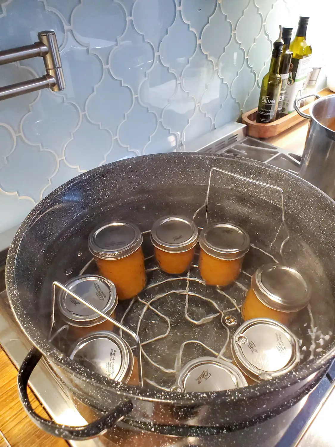 A large canning pot on the stove boiling away with eight jars of preserves enduring the hot bath canning process. 