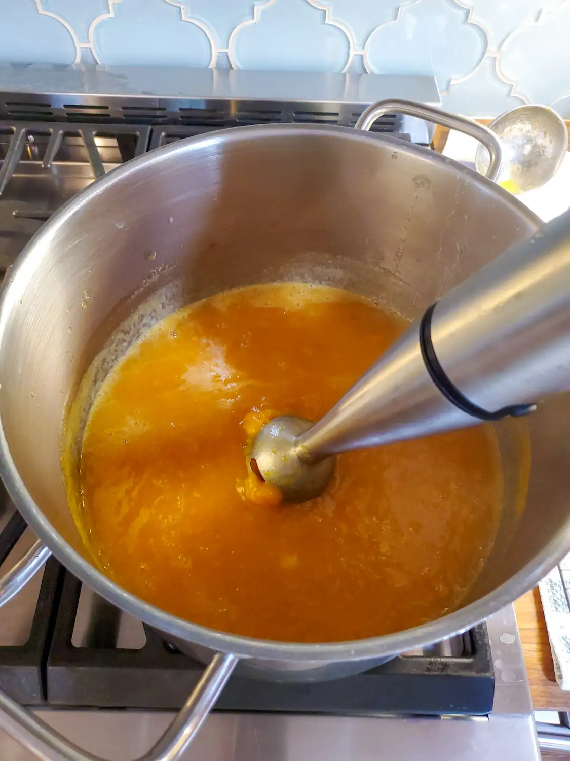 An immersion blender is being used to blend the peach mixture in a stock pot on the stove. 
