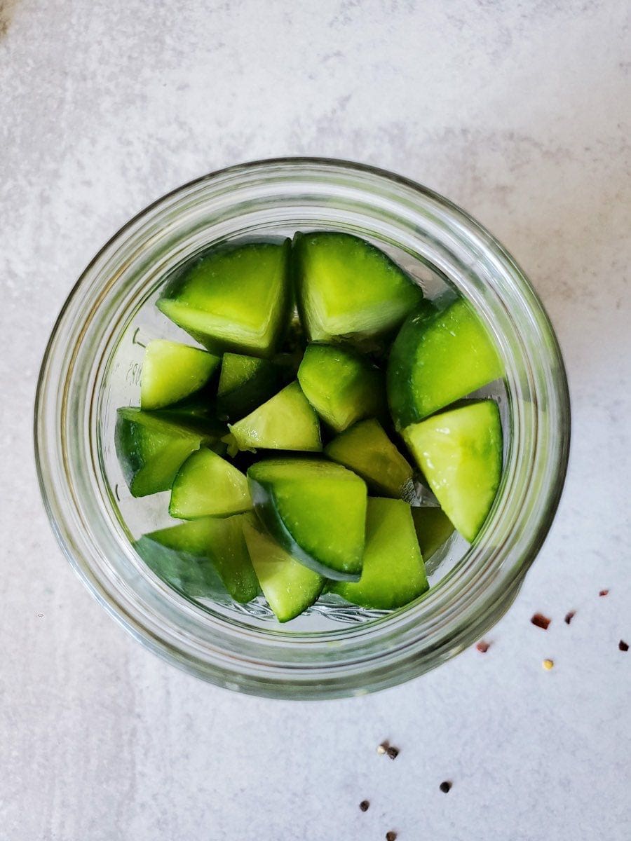 An image from above of a mason jar that as been filled with vertically stacked cucumber halves. 