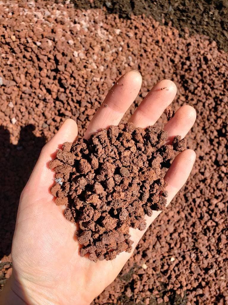 A hand holding small red lava rock pieces, that are being added to the new raised bed. 