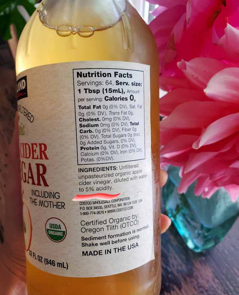 A close up image of a bottle of apple cider vinegar. A red line has been superimposed on the bottle underneath the "5% acidity" labeling to illustrate what to look for in vinegar. 
