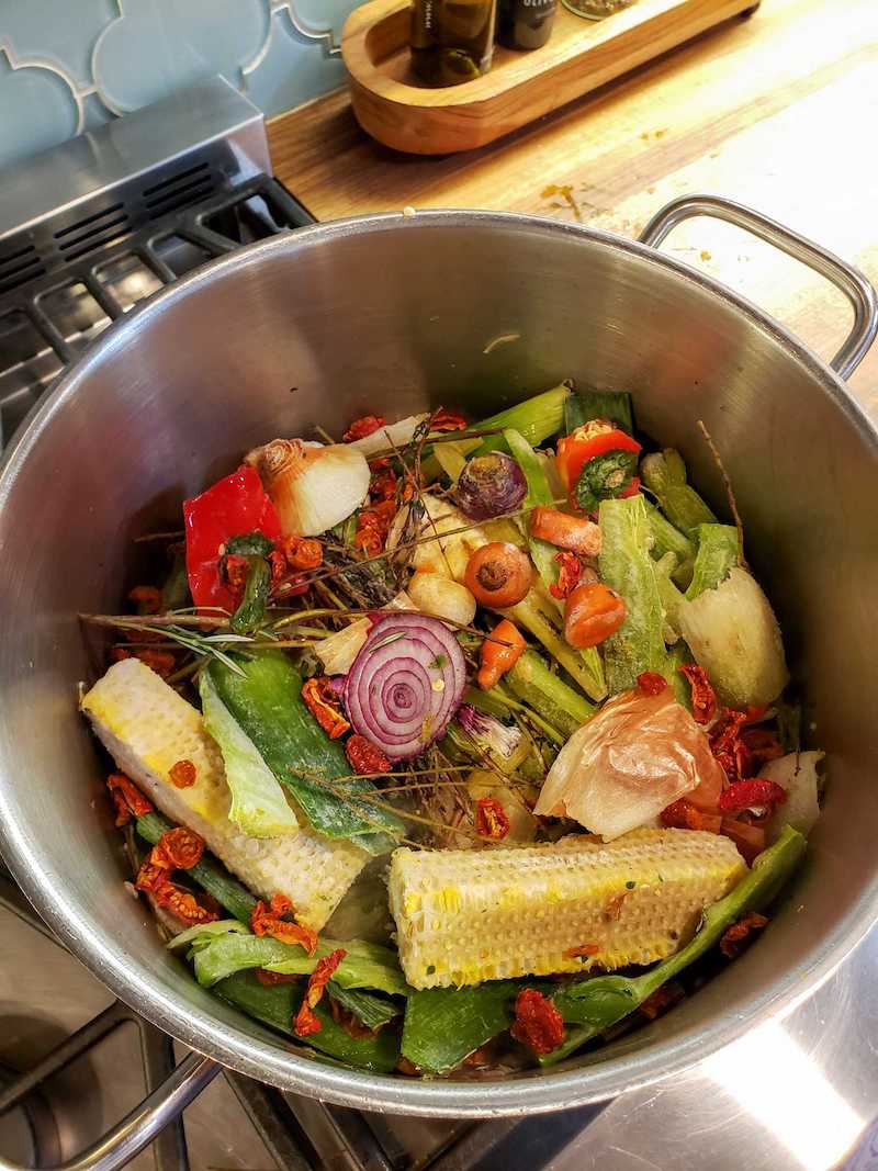 The frozen vegetable scraps have been added on top of the fresh and sautéed scraps inside the stock pot before water is added. 