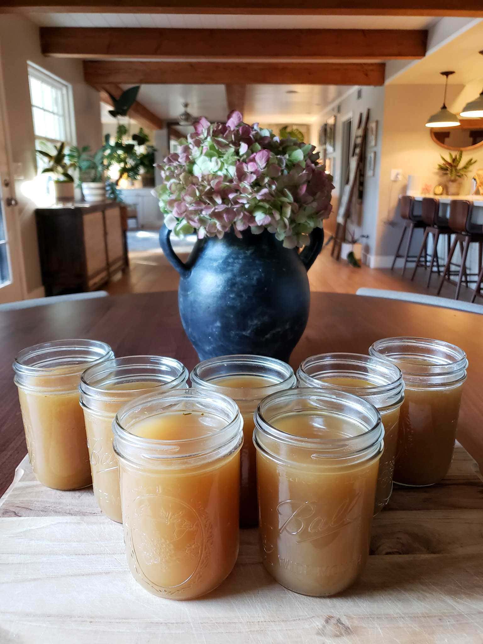 Seven pint jars of vegetable broth lined up like bowing pins on a wooden cutting board. The liquid is light brown in color.