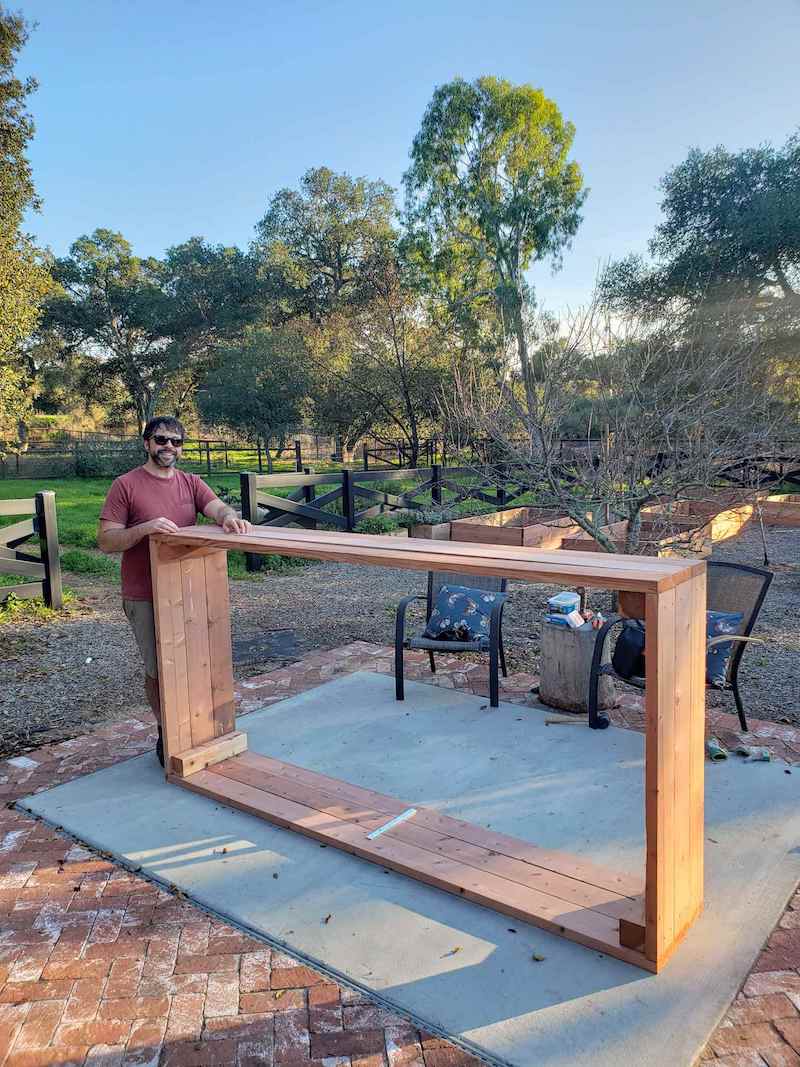 Aaron is standing next toe a built garden bed that is tipped on its side, the only remaining step is to seal the wood with garden safe sealant and add hardware cloth to the bottom. 