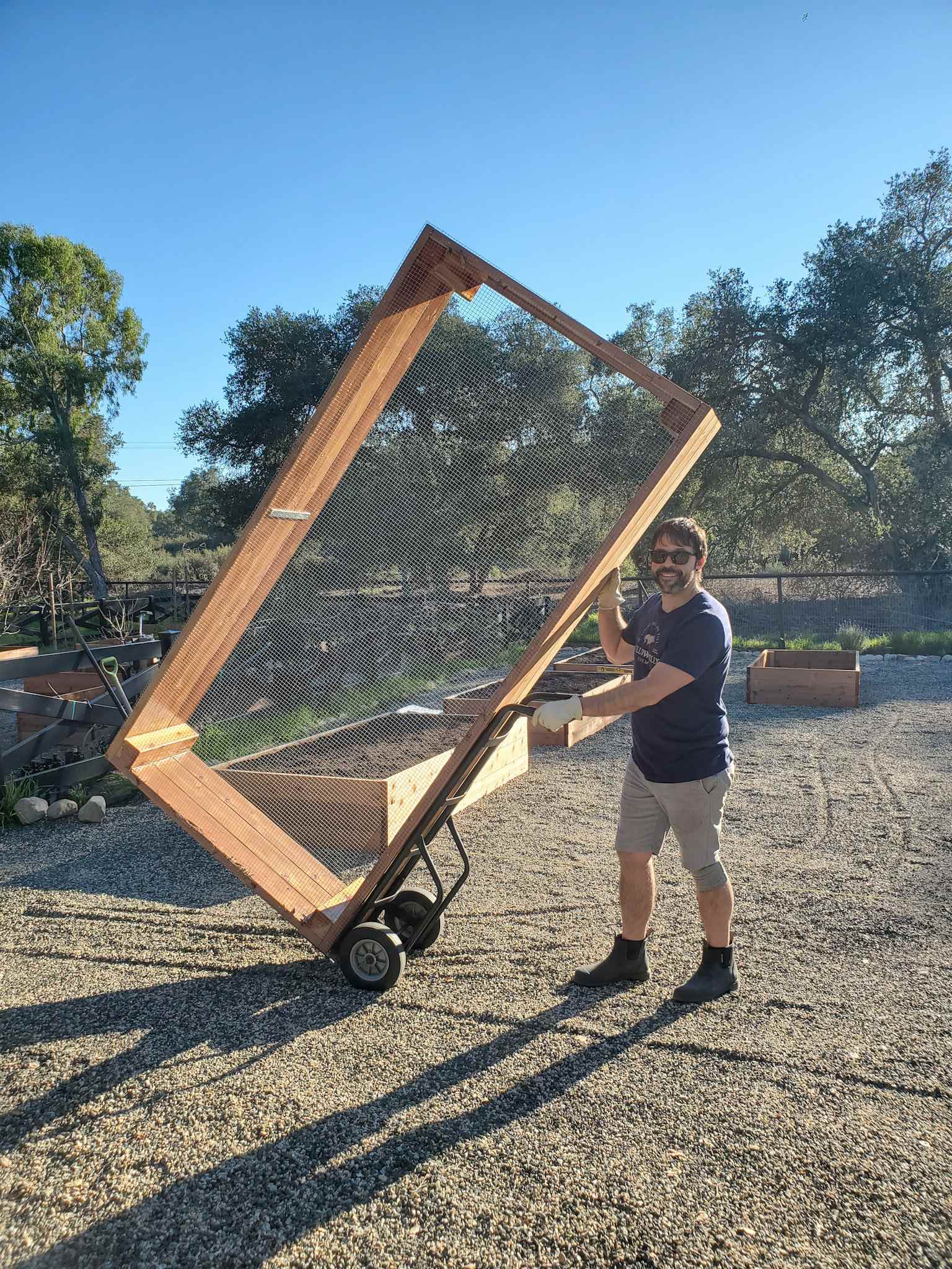 Aaron is using a hand truck to move a 8x4 raised garden bed into position in the new garden space. 