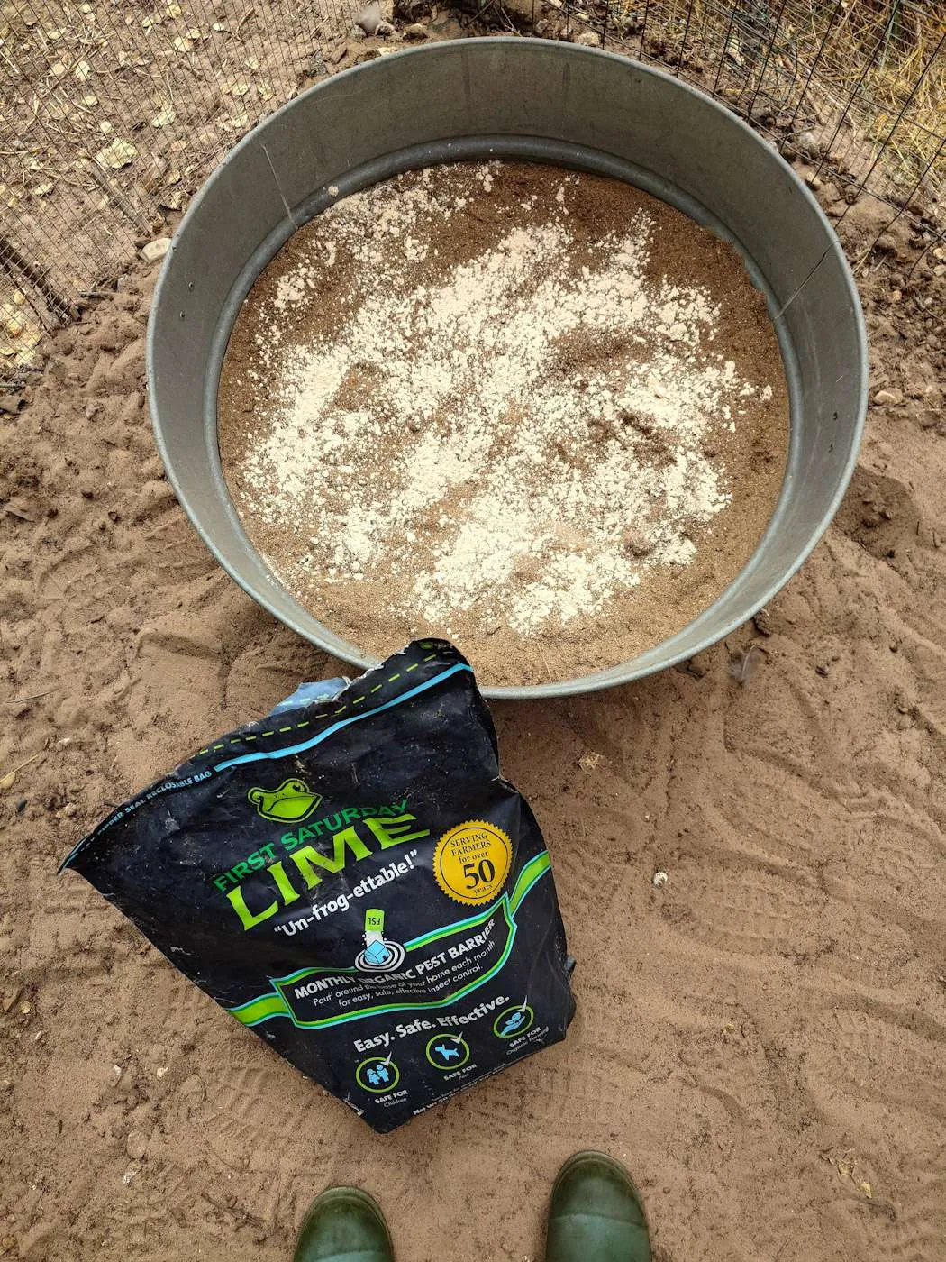 A metal tub is full of dirt and sand with a sprinkle of lime on top which will be mixed into the soil and sand. The bag of lime sits just outside the tub to illustrate the brand of lime used. 