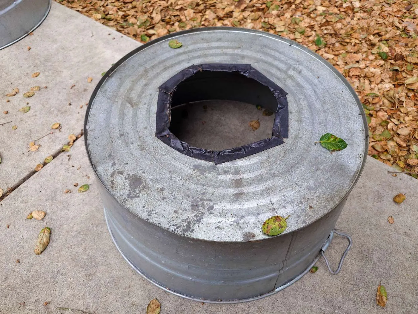A metal tub is shown upside down, the bottom of the tub has a large hole cut out of the bottom and the edges of the hole have been lined with duct tape to protect from the sharp edges. 