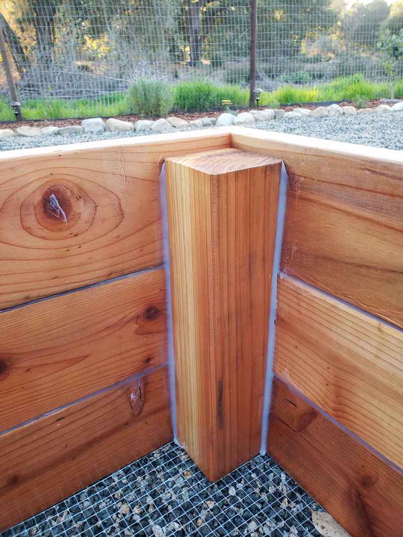 The corner of the inside of a raised bed is shown, the seams in between the 4x4 and 2x6 boards are sealed with sealant. 