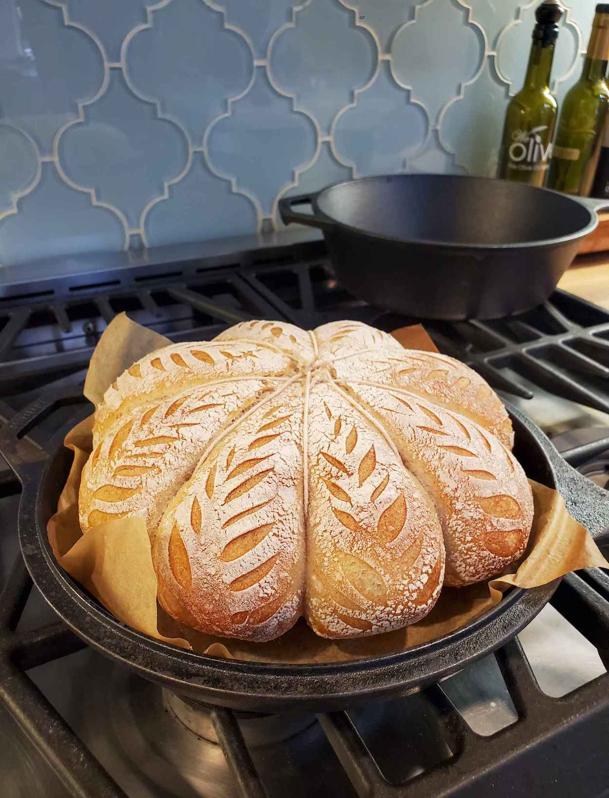 A baked loaf of sourdough sits in the bottom part of a cast iron combo cooker after being removed from the oven. The top half or lid portion has been removed to reveal the beautiful bread inside. 