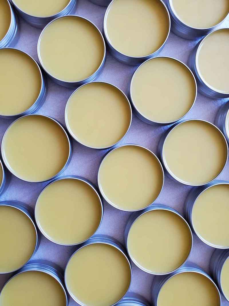 A birds eye view of many metal tins full of balm laid out with tins left to right and up and down from each tin. 