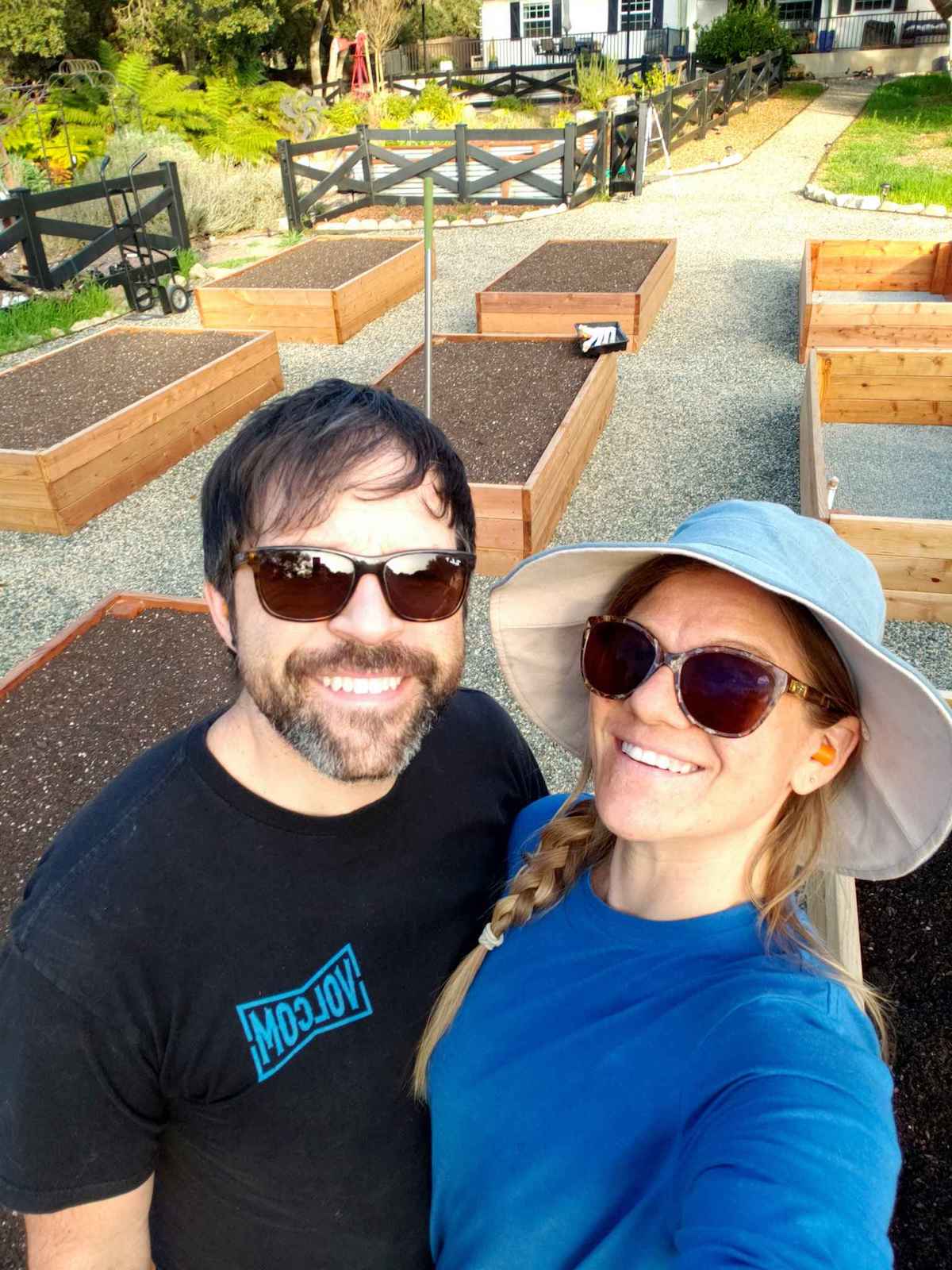 Aaron and Deanna taking a selfie standing in front of their new garden area that is in the process of being created.