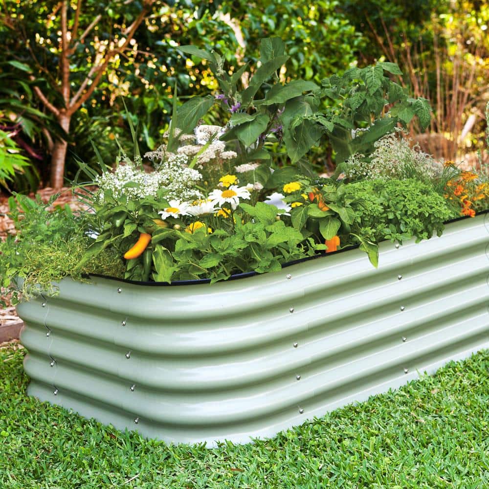 A long rectangular corrugated galvanized metal raised garden bed is sitting on grass. There are various flowers, herbs, perennials, and pepper plants planted amongst the bed. 