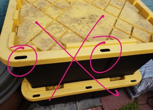An image of a black storage tote with yellow lid, that has some holes around the outer edge of the lid. This is an example of what type of bin not to get. The holes are circled in the photo. 